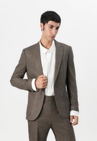 Brun rutig kostym med skräddarsydd passform, med notch-krage, två framfickor och en vit button-down skjorta under.