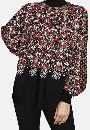 Løs bluse med indviklede geometriske og blomsteragtige mønstre i sort, hvid og rød, lange puffede ærmer og sorte tætsiddende manchetter og kant.