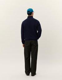 Giacca in fleece navy con zip e colletto, abbinata a pantaloni in denim scuro e un berretto blu brillante. Il tessuto appare morbido e strutturato.