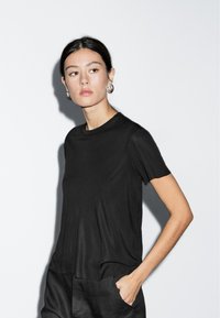 Sort T-shirt med korte ærmer og rund halsudskæring, afslappet pasform, lavet af blødt stof, kombineret med løstsiddende, mørke bukser.