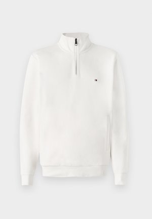 Bela dukserica s visokim ovratnikom i zatvaranjem na pola zatvarača, ima mali logo na prsima i rebraste rukave. Mehak, gladek material.