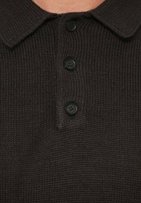 Polo de punto marrón con tejido texturizado, un collar y tres cierres de botón negro en el cuello.