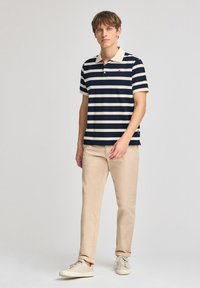 Marinblå och vit randig polo skjorta med en beige krage, med en liten logotyp på vänster bröst och parat med ljusbeige chinos och sneakers.