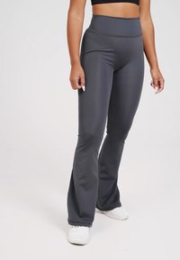 Leggings grigi alti a vita alta svasati, realizzati in un tessuto elasticizzato, caratterizzati da una superficie liscia e un design aderente, abbinati a scarpe da ginnastica bianche.