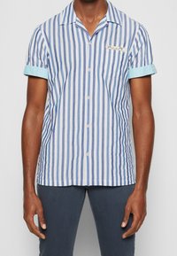 Camisa de manga corta con botones en rayas verticales azul y blanco, con puño azul claro, bolsillo de tela y diseño de cuello.