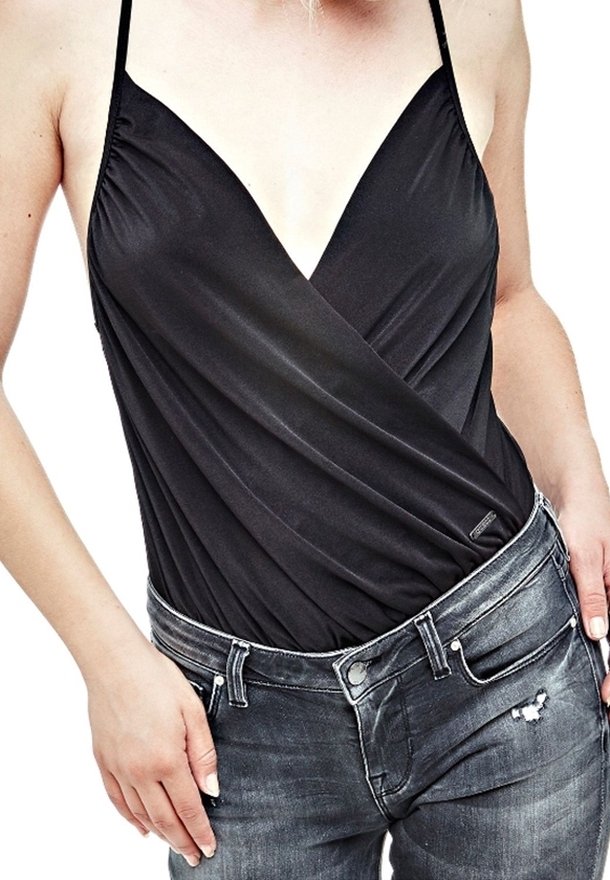 Body noir enveloppant avec des fines bretelles, présentant un décolleté en V profond et un tissu drapé. Associé à un jean gris déchiré.