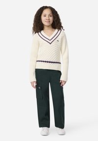 Εκρού πλεκτό πουλόβερ με V-λαιμόκοψη, διακοσμημένο με υφή και ναυτικό ριγέ σχέδιο. Συνδυασμένο με σκούρο πράσινο παντελόνι cargo και λευκά αθλητικά παπούτσια.