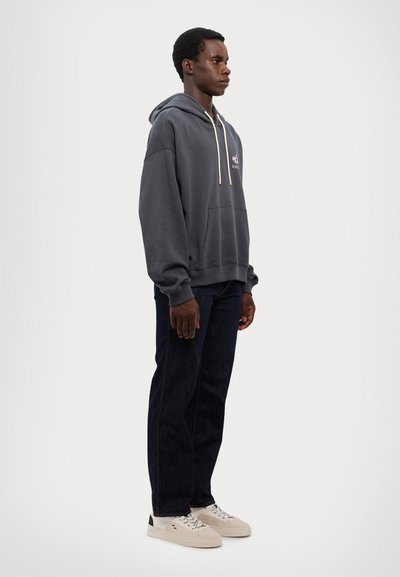 Sweat à capuche gris foncé avec une poche avant, détail du logo rose et cordon de serrage ajustable. Associé à un jean foncé et des baskets claires.