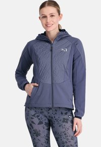 Haut à zip marine avec un design texturé à l'avant, poches latérales et une capuche ajustée. Associé à des leggings à motif floral.