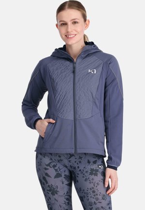 Marineblauwe zip-up hoodie met een oppervlaktestructuur aan de voorkant, zijzakken en een aansluitende capuchon. Gepaard met leggings met bloemmotief.