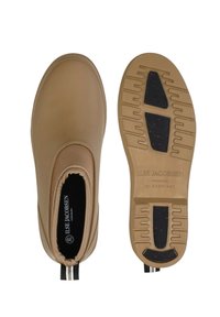 Beżowe wodoodporne buty wsuwane z gładką cholewką, czarną wyściółką oraz teksturowaną gumową podeszwą z czerwonymi kropkami i pętelką do ściągania.