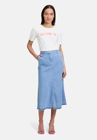 Lichtblauwe spijkerrok met een hoge taille, frontnaaddetails en zakken. Gecombineerd met een wit graphic t-shirt en roze sandalen.