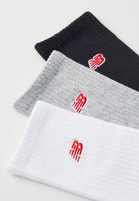 Tre par ribbede sokker i sort, grå og hvid, hver med et rødt broderet logo. Blødt stof med en tekstureret overflade.