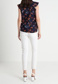Marinblomstrig blus med volangärmar, matchad med vita smala jeans och ankelskor med klack. Har färgglada blommönster på tyget.