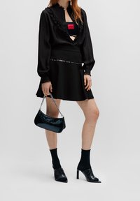 Zwarte blouse met gerimpelde kraag, gelaagd over een zwarte croptop. Zwarte wijde rok met studded riem, gecombineerd met zwarte muiltjes en een glanzende handtas.