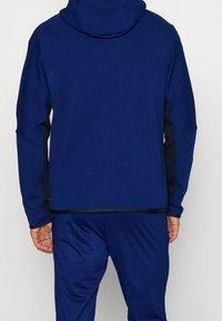 Felpa con cappuccio blu navy con dettagli neri sulle maniche. Tessuto morbido, vestibilità comoda e design semplice. Cuciture visibili.