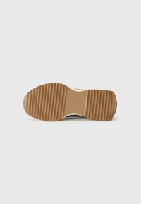 Semelle de chaussure présentant une texture striée en caoutchouc brun clair avec une forme courbée et des accents beige. Conception plate et robuste pour une bonne traction.