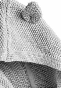 Cappuccio grigio lavorato a maglia con un motivo testurizzato, caratterizzato da un piccolo dettaglio ad anello nella parte superiore e un bordo liscio attorno al collo.