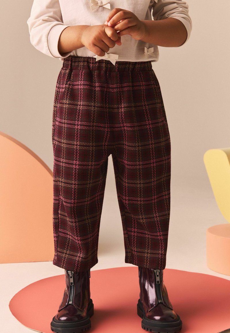 Pantalones de cuadros en burdeos oscuro con acentos en amarillo y rosa, que cuentan con una cintura elástica y piernas ajustadas, combinados con botas negras brillantes con cremallera.