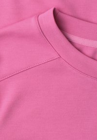 Gros plan d’un sweat-shirt rose à col rond montrant le col, la couture et la texture douce du tissu en coton.