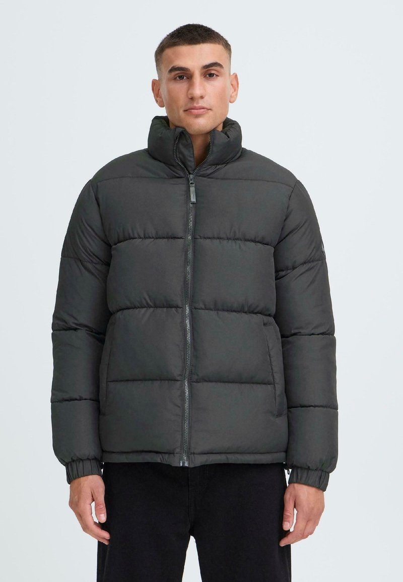 Mörkgrå puffjacka med hög krage, plisserad design, framzipper och elastiska ärmar. Har en slät, matt yta.