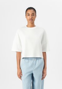 White cropped t-shirt made from soft fabric, featuring short sleeves and a round neckline, paired with light blue, elastic-waist pants.