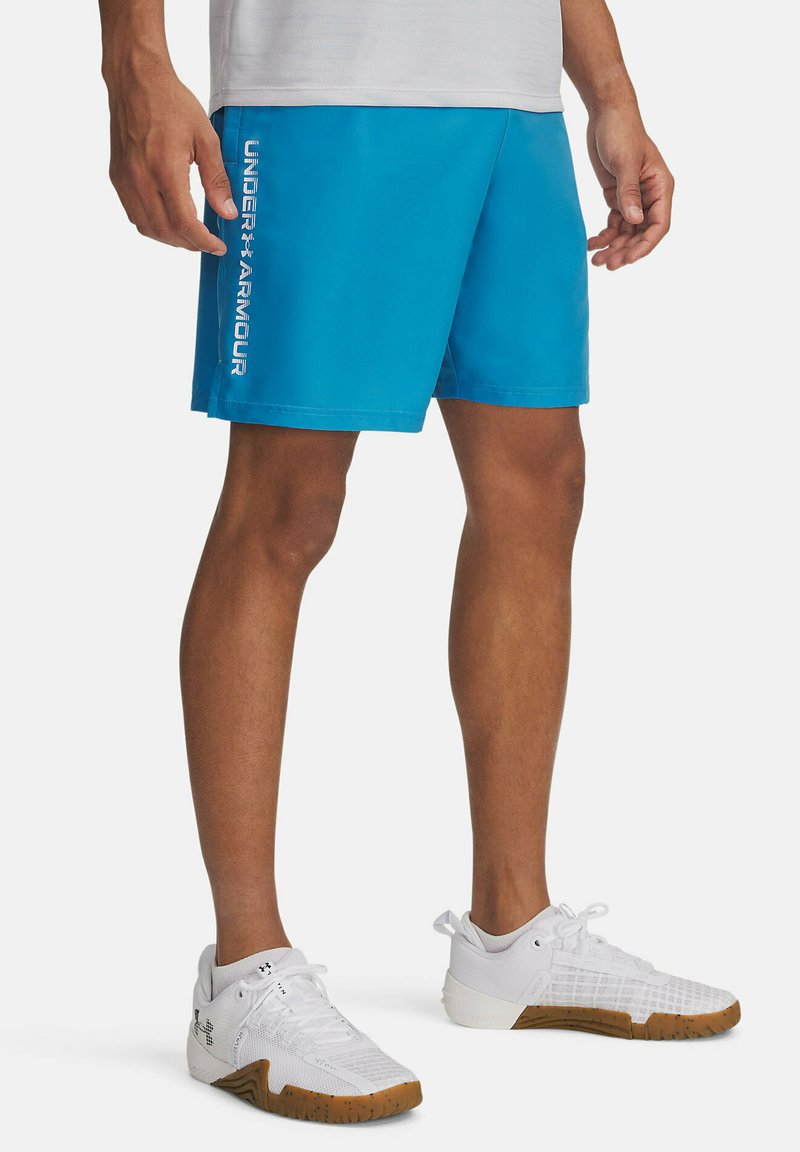Blauwe atletische shorts gemaakt van een lichtgewicht materiaal, met een gedurfde witte "UNDER ARMOUR" logo aan de zijkant. Draagt witte sneakers.