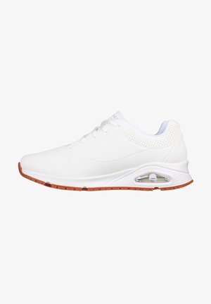 Scarpe sportive bianche con una tomaia in sintetico liscio, dettagli perforati e suola in gomma color nocciola con un'unità di ammortizzazione d'aria visibile.