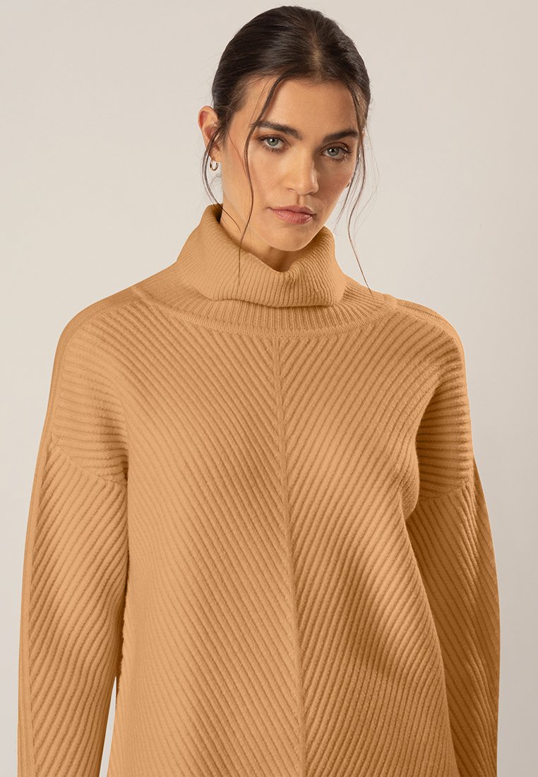 Beige Rollkragenpullover mit diagonaler Rippstruktur, lockerer Passform und langen Ärmeln. Verfügt über einen hohen Kragen und subtile Nähdetails.
