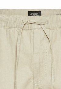 Beige elastiske shorts med snoretræk, der har en ensartet tekstur og sidelommer. Mærket "Camel Active" er synligt på taljebåndet.