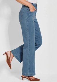 Helleblaue Jeans aus Denim mit geradem Bein, zwei hinteren Taschen und minimalem Nähdetail, kombiniert mit braunen Absatzschuhen.