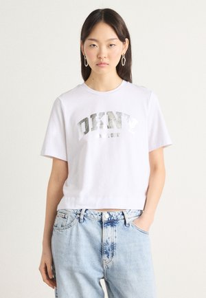 Hvit kort t-skjorte med et sølvreflekterende "DKNY NEW YORK" grafikk. Kombinert med lyseblå slitte jeans. Enkel, avslappet design.