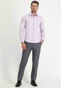 Una camicia a maniche lunghe di colore viola chiaro con chiusura a bottoni, abbinata a pantaloni grigi e scarpe in pelle nera, indossata da un modello maschile.