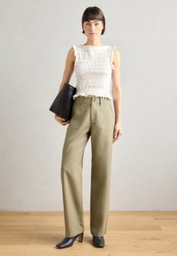Pantalon en coton vert olive avec des jambes larges et des poches avant, associé à un haut blanc texturé à volants et un sac à main noir.