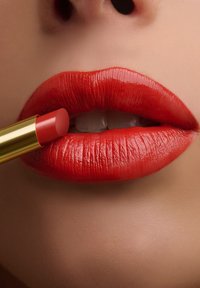 Primo piano di labbra con rossetto rosso lucido applicato con un rossetto rosso in una confezione dorata.