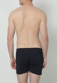 Zwarte katoenen boxershorts met een elastische tailleband, gezien van achteren. De stof lijkt zacht en soepel met een strakke pasvorm.