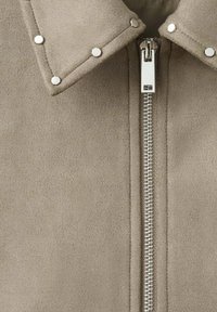 Jachetă din piele ecologică tip șuviță taupe, cu închidere cu fermoar, decorată cu ținte argintii pe guler și un fermoar metalic în partea din față.