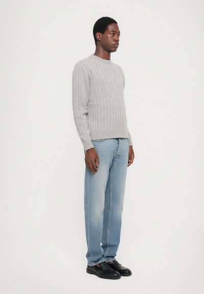 Pulover din tricot gri deschis cu model canelat, cu gât rotund, asortat cu jeans albastri uzați, drepti, și încălțăminte neagră. Design simplu și funcțional.