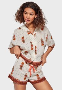 Conjunto de pijama con estampado floral que incluye una camiseta de manga corta y pantalones cortos con cintura elástica en color crema con lunares, acentuado con una banda decorativa.
