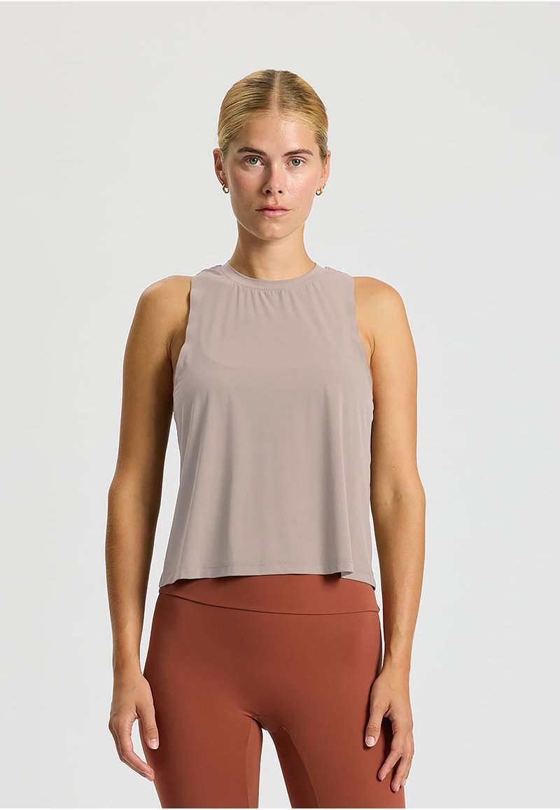 Top senza maniche color taupe chiaro con scollatura rotonda. Vestibilità fluida e texture liscia, abbinato a leggings color ruggine. Nessun motivo o hardware notevole.