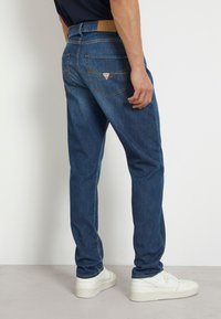 Jeans in denim blu con un design a gamba dritta, tessuto testurizzato e due tasche posteriori con un'etichetta a forma di triangolo.