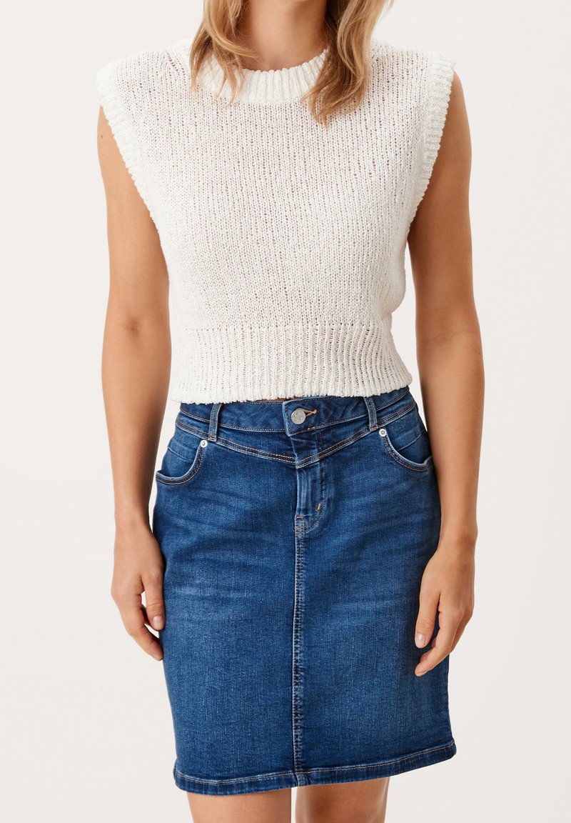 Top blanco de punto sin mangas con dobladillo acanalado, combinado con una falda de mezclilla azul ajustada que presenta bolsillos delanteros y costuras visibles.