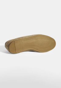 Beige durchlöcherter Sneaker mit einem Obermaterial aus Textil, einer festen Gummi-Außensohle und einer ausgeprägten runden Zehenform. Sichtbare Nähte setzen Akzente.