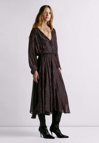 Long, black dress with multicolored vertical stripes. Features a v-neck, long sleeves, cinched waist, and a flowing skirt. Worn with high black boots.
