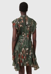 Floral print dress in dark green, featuring short flutter sleeves, a zip closure at the back, and a flowing skirt with pleat detail.