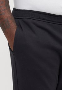 Schwarze Jogginghose mit elastischem Bund und Seitentaschen. Hergestellt aus weichem Baumwollmischmaterial; glatte Textur und lässiges Design.