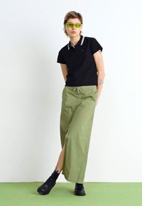 Čierna polo tričko s bielym golierom, svetlozelené široké nohavice, zelené slnečné okuliare a čierne topánky. Hladká tkanina, uvoľnený strih.