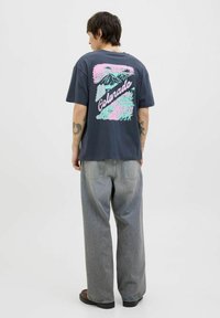 Mørkegrå bomulds t-shirt med en farverig "Colorado" grafik, der viser bjerge og træer, parret med lysegrå løse jeans.
