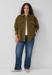 Olijfgroene corduroy overhemd met knoopsluiting, twee borstzakken, opgerolde mouwen; gecombineerd met blauwe rechte jeans en beige ballerina's.