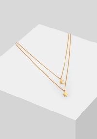 Collana a strati in tono oro con pendente a forma di luna crescente e stella. Le catene presentano una texture delicata e fine con una finitura lucida.